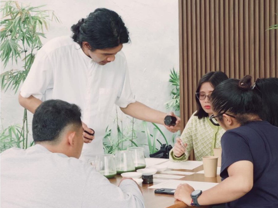 The owner leading a tasting session with his baristas around a table of cupping glasses